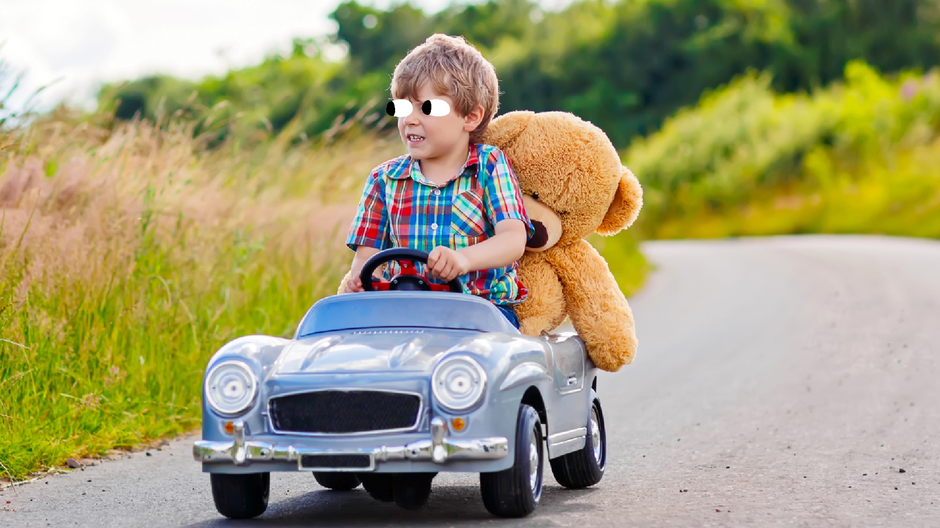 A child driving a miniature car with a teddy in the back
