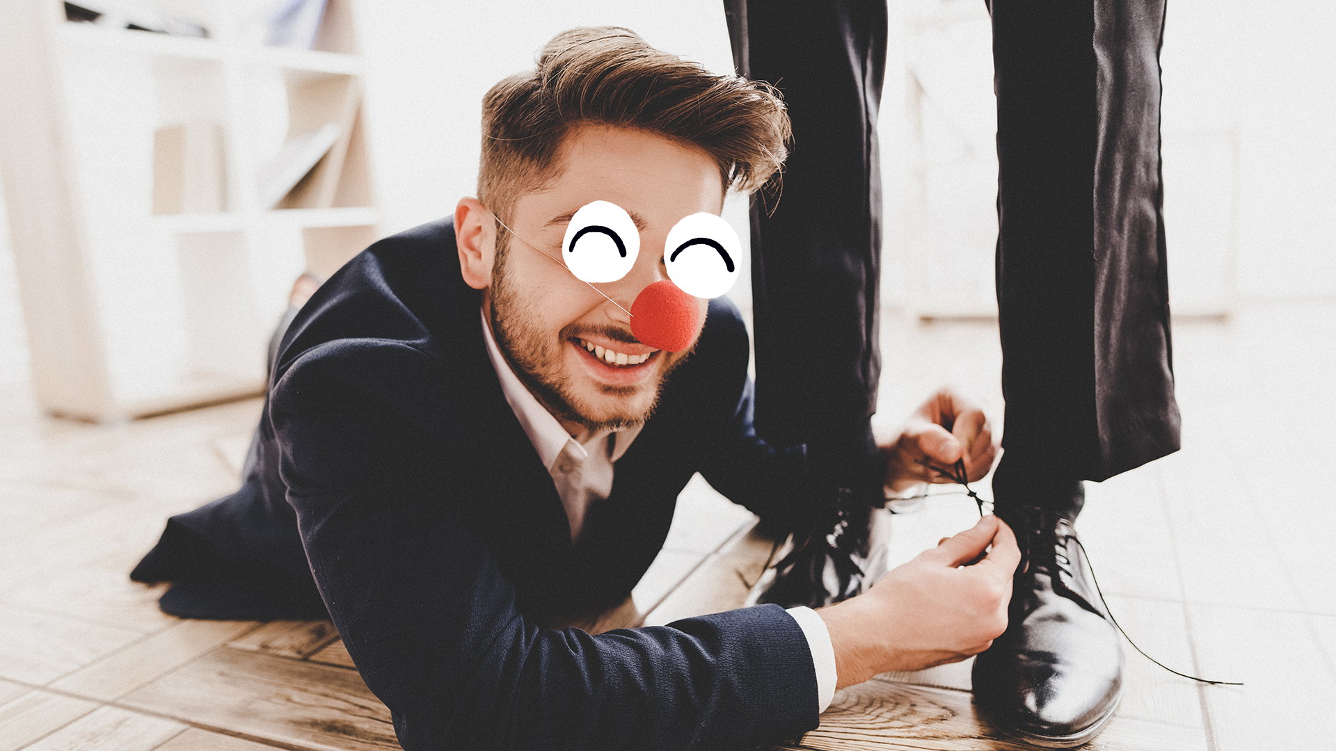 A man with a clown's nose tying their friend's shoes together for a dangerous prank