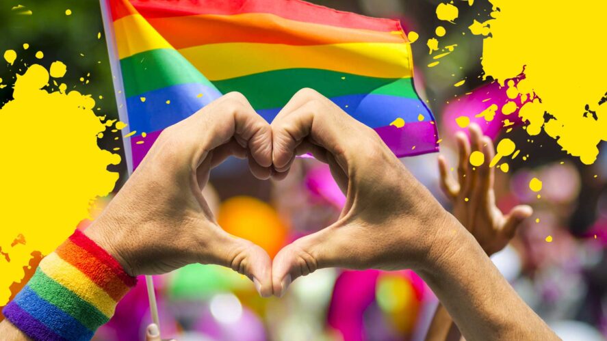 A Pride parade with a man making a heart shape with his hands