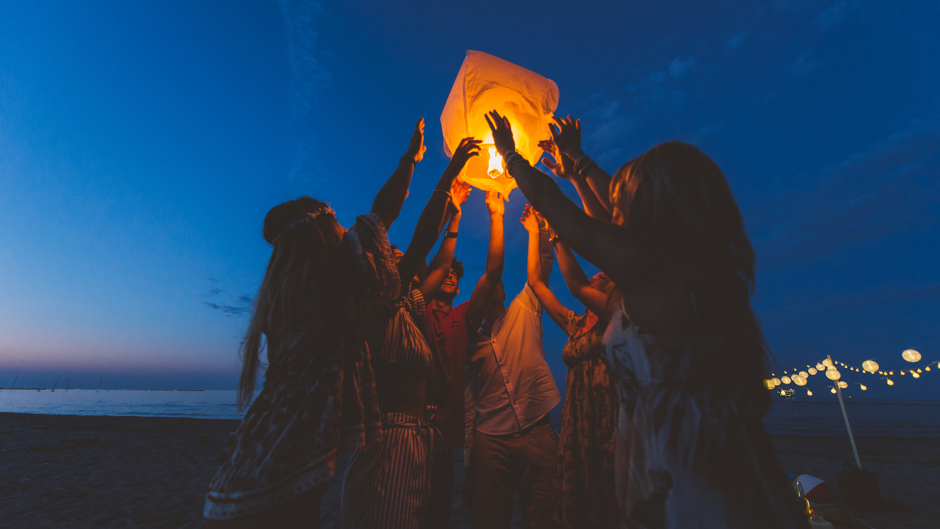 A group of girls lighting a lantern on a beach